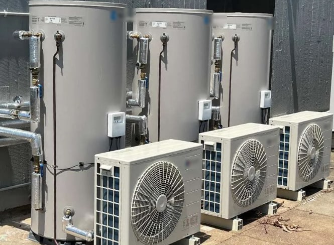Three separate split heat pump water heater systems installed side by side, each with its own storage tank and small outdoor heat pump unit.