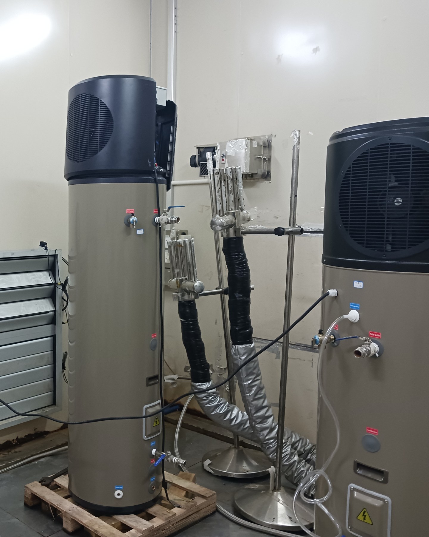 Two heat pump water heaters connected for testing in a laboratory, with insulated ducts and sensor stands
